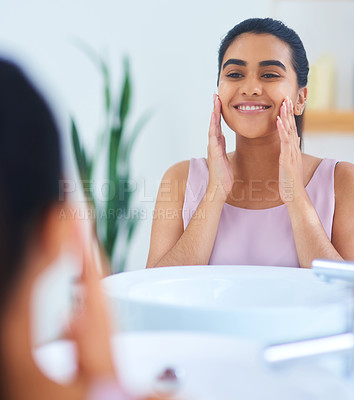 Buy stock photo Shot of a young woman applying moisturiser to her face in a bathroom at home