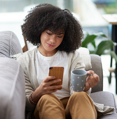 Buy stock photo Shot of a young woman using a cellphone while relaxing on a sofa at home