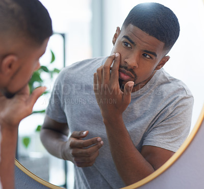 Buy stock photo Cropped shot of a handsome young man standing and looking at his skin in his bathroom mirror