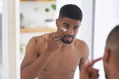 Buy stock photo Cropped shot of a handsome young man standing and using his bathroom mirror to apply moisturizer on his face