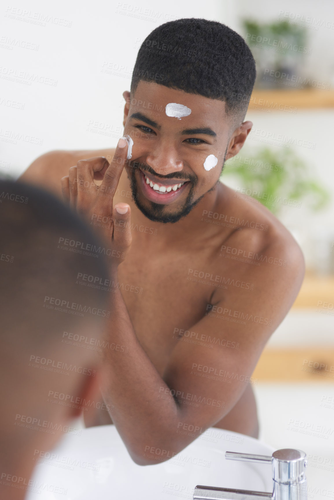 Buy stock photo Cropped shot of a handsome young man standing and using his bathroom mirror to apply moisturizer on his face