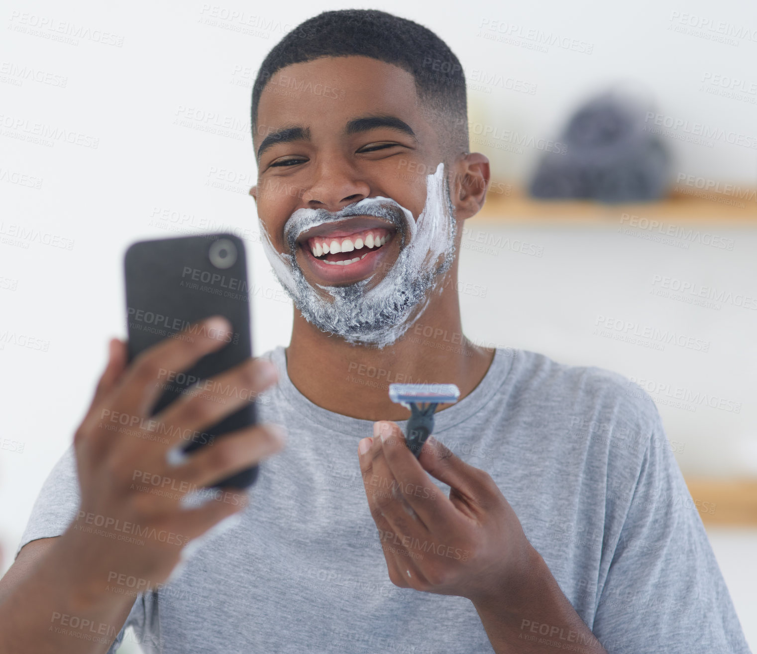 Buy stock photo Cropped shot of a handsome young man standing and using his cellphone to vlog while shaving in the morning