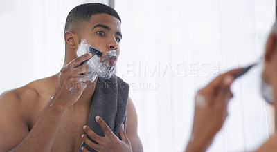 Buy stock photo Cropped shot of a handsome young man standing and using his bathroom mirror to shave in the morning