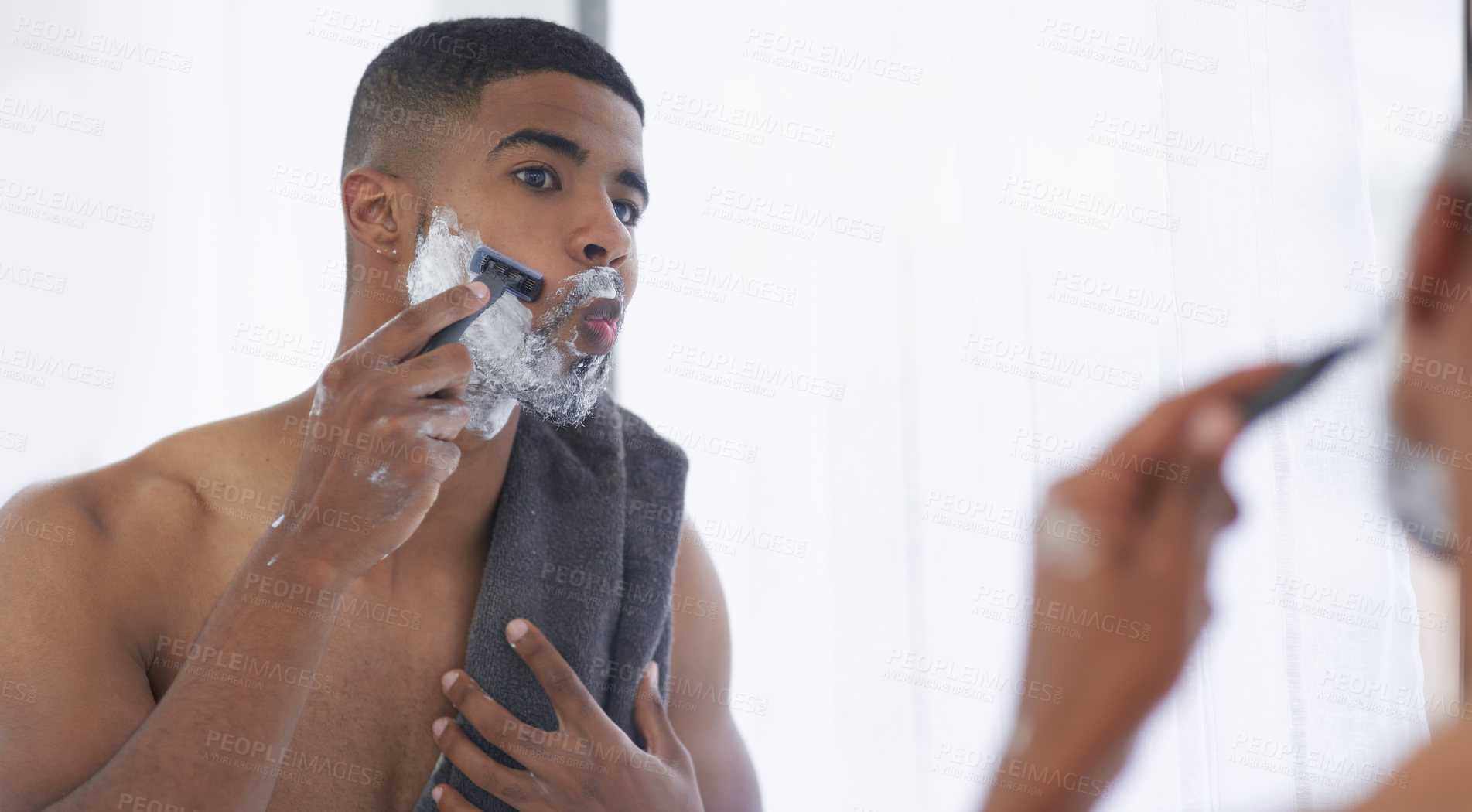 Buy stock photo Cropped shot of a handsome young man standing and using his bathroom mirror to shave in the morning