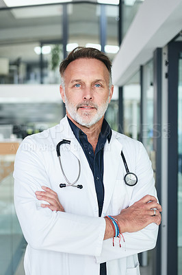 Buy stock photo Cropped portrait of a handsome mature doctor standing with his arms folded in the clinic during the day