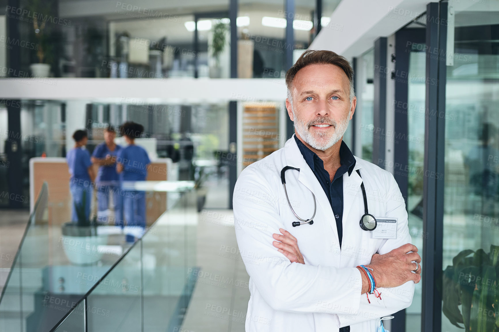 Buy stock photo Cropped portrait of a handsome mature doctor standing with his arms folded in the clinic during the day