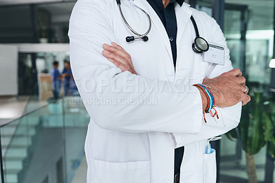 Buy stock photo Cropped shot of an unrecognizable doctor standing with his arms folded in the clinic during the day
