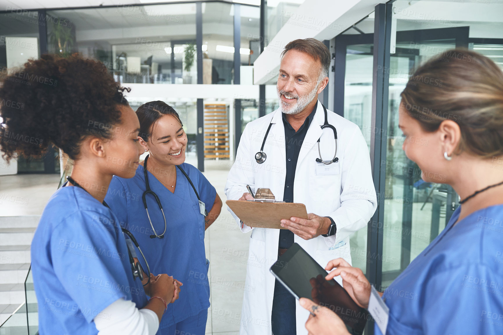 Buy stock photo Cropped shot of a handsome mature doctor standing with his nurses and having a discussion in the clinic