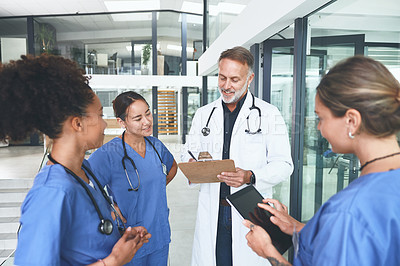 Buy stock photo Cropped shot of a handsome mature doctor standing with his nurses and having a discussion in the clinic