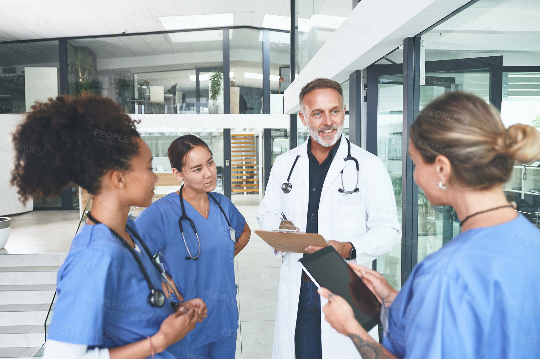 Buy stock photo Cropped shot of a handsome mature doctor standing with his nurses and having a discussion in the clinic