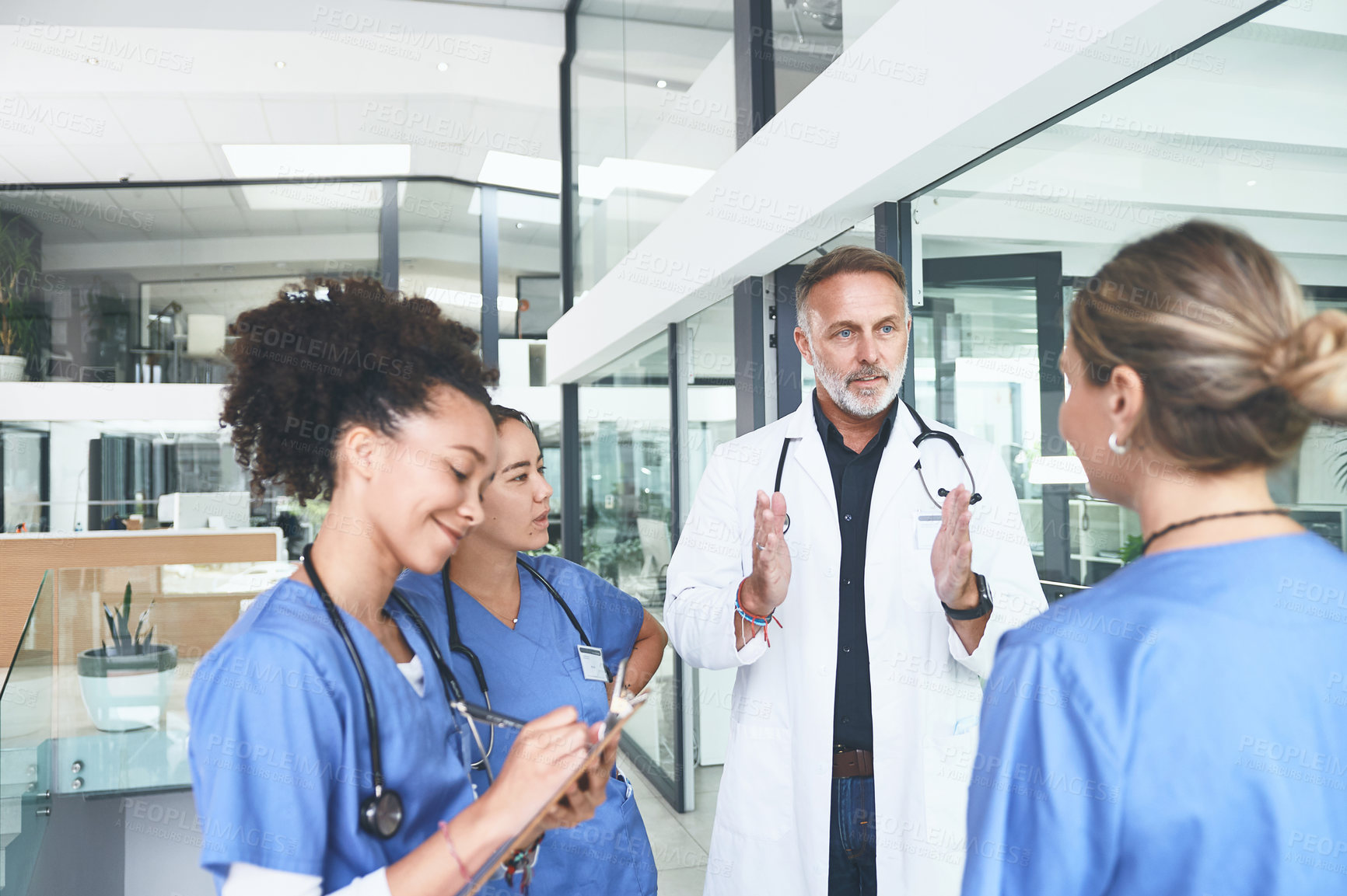 Buy stock photo Cropped shot of a handsome mature doctor standing with his nurses and having a discussion in the clinic