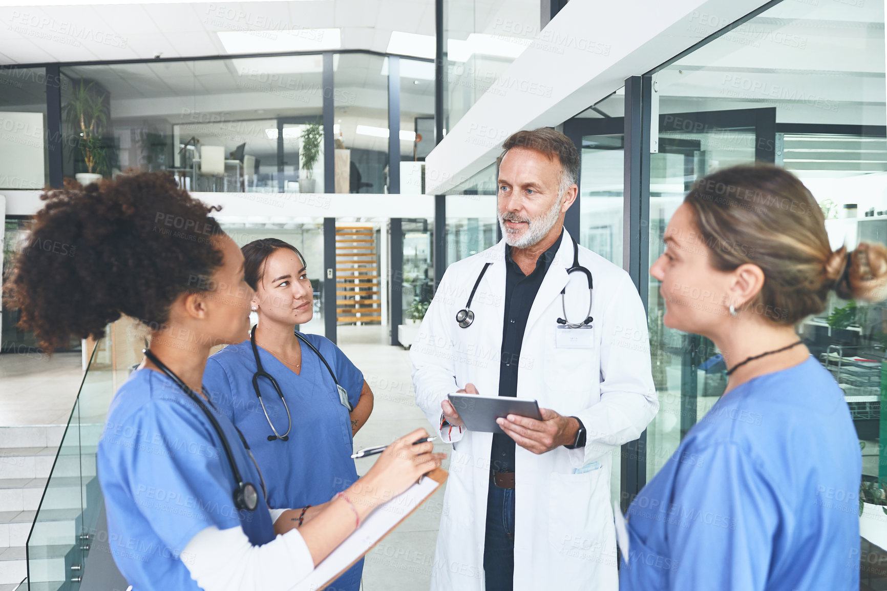 Buy stock photo Cropped shot of a handsome mature doctor standing with his nurses and using a digital tablet during a discussion