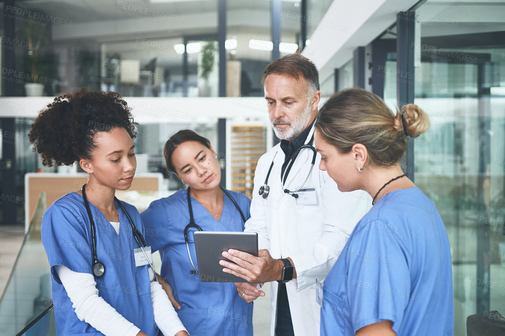 Buy stock photo Cropped shot of a handsome mature doctor standing with his nurses and using a digital tablet during a discussion