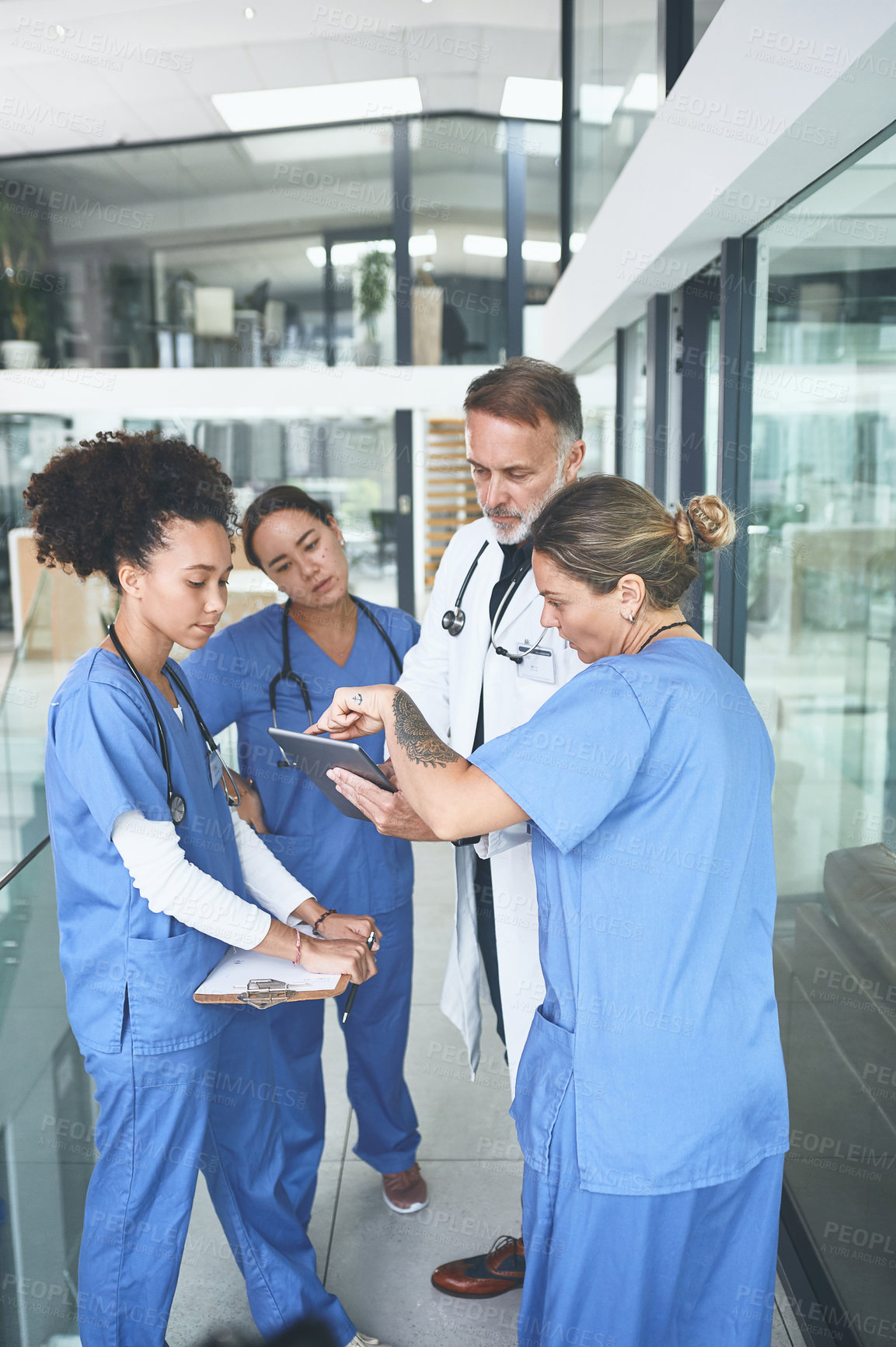 Buy stock photo Cropped shot of a handsome mature doctor standing with his nurses and using a digital tablet during a discussion