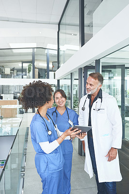 Buy stock photo Cropped shot of a handsome mature doctor standing with his nurses and using a digital tablet during a discussion