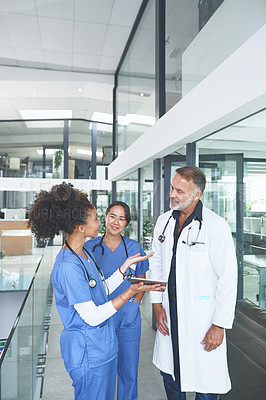 Buy stock photo Cropped shot of a handsome mature doctor standing with his nurses and using a digital tablet during a discussion