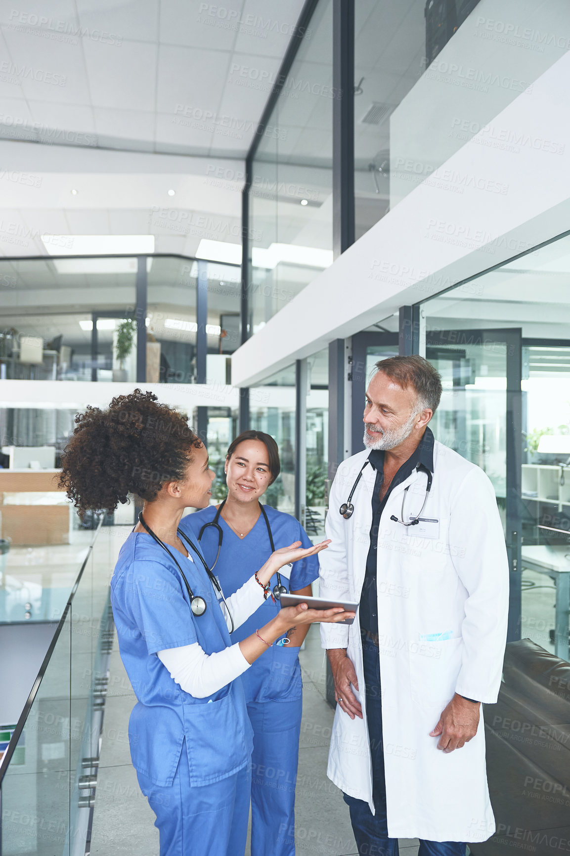 Buy stock photo Cropped shot of a handsome mature doctor standing with his nurses and using a digital tablet during a discussion