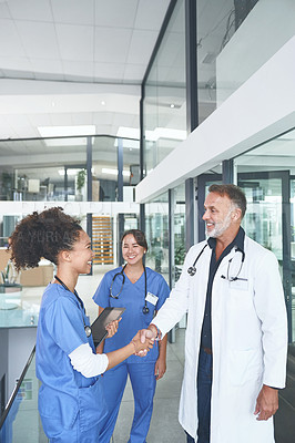 Buy stock photo Cropped shot of a handsome mature doctor standing and shaking a nurse's hand in the clinic