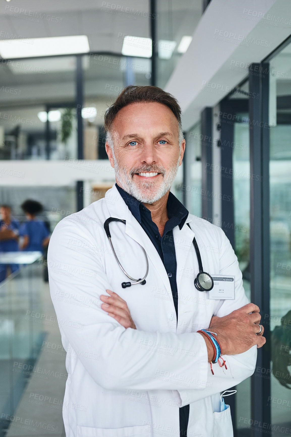 Buy stock photo Cropped portrait of a handsome mature doctor standing with his arms folded in the clinic during the day