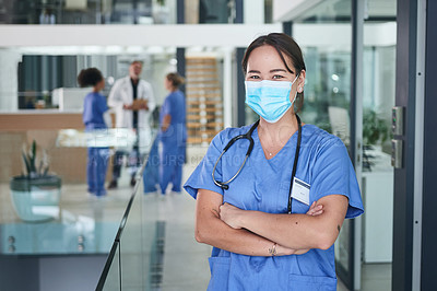 Buy stock photo Cropped portrait of an attractive young nurse wearing a face mask and standing in the clinic with her arms folded