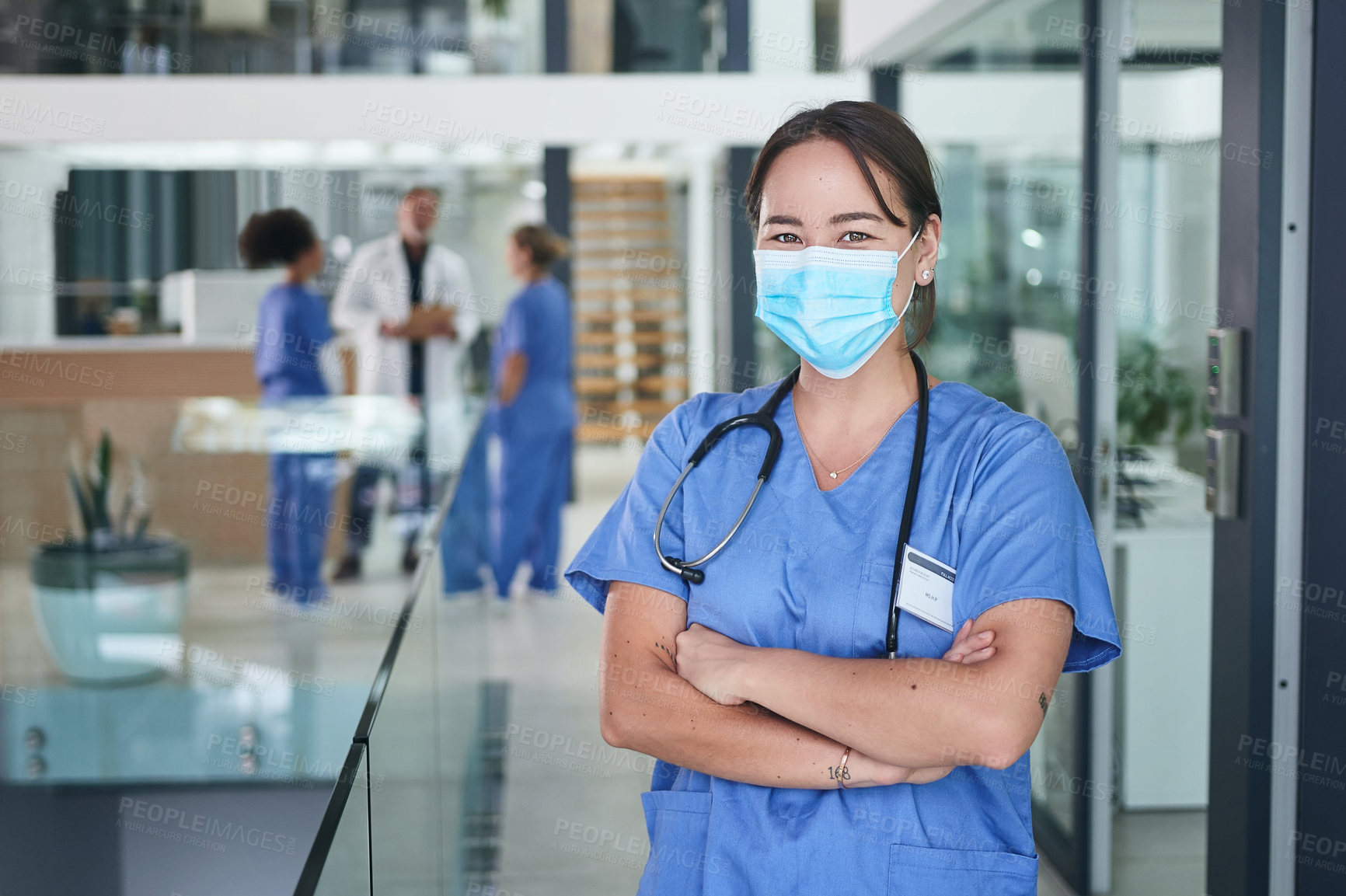 Buy stock photo Cropped portrait of an attractive young nurse wearing a face mask and standing in the clinic with her arms folded