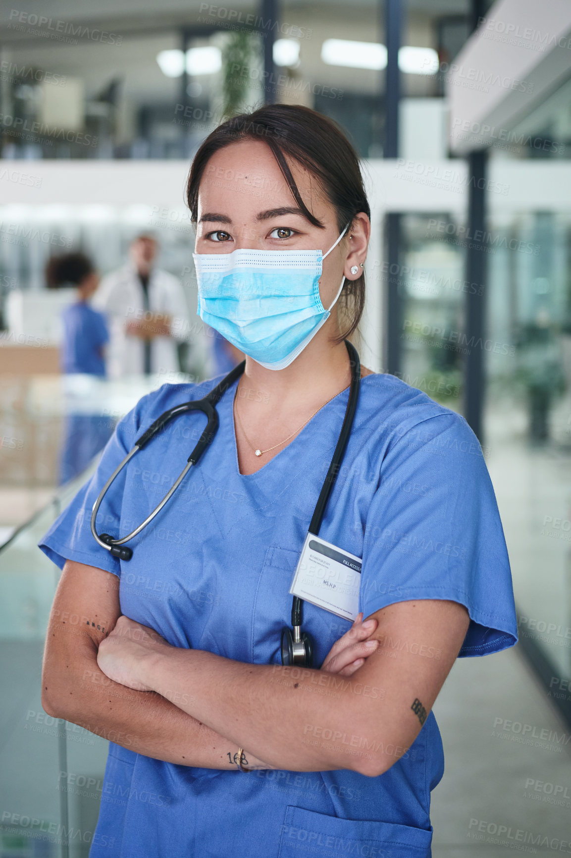 Buy stock photo Cropped portrait of an attractive young nurse wearing a face mask and standing in the clinic with her arms folded