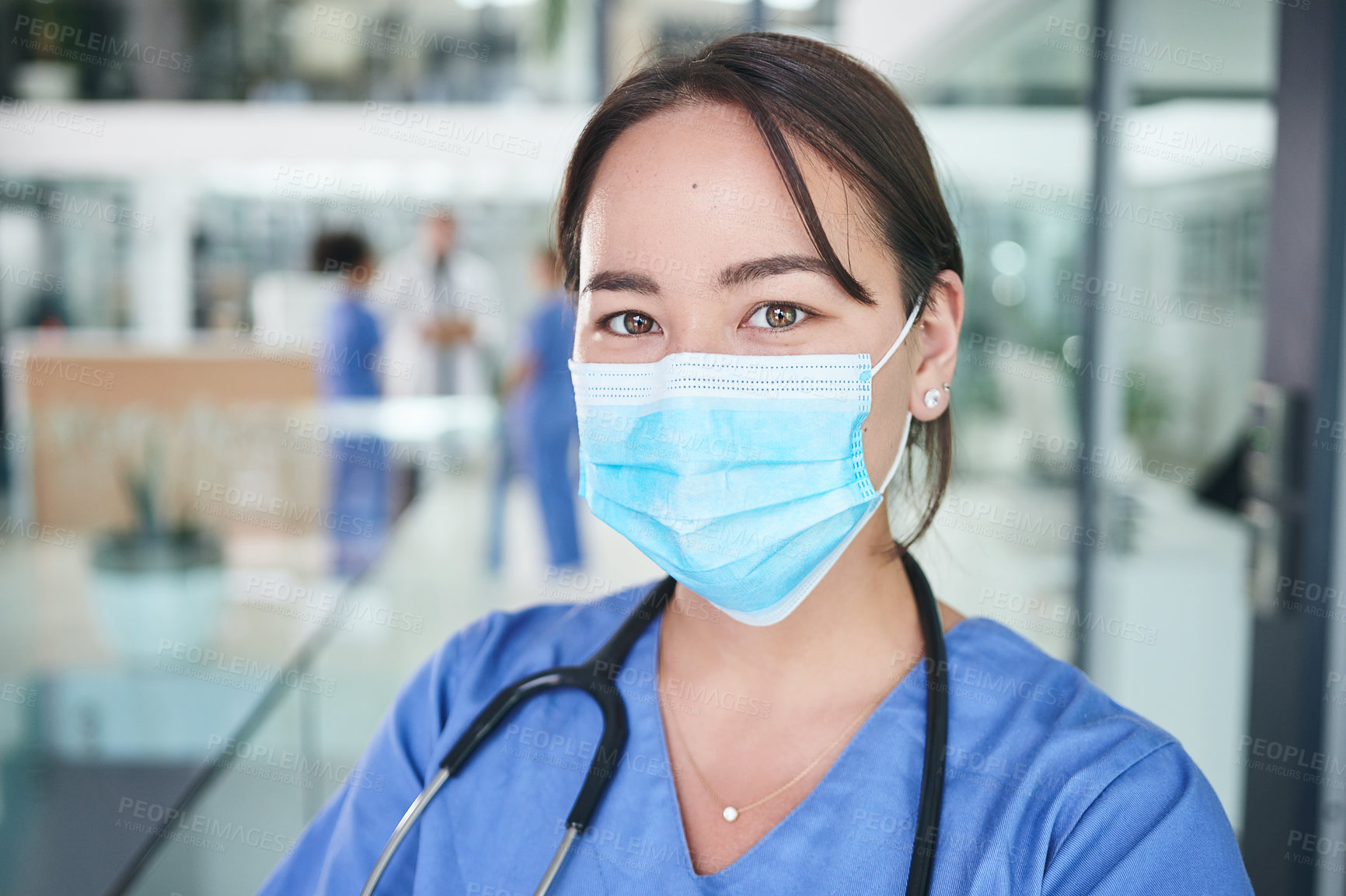 Buy stock photo Cropped portrait of an attractive young nurse wearing a face mask and standing in the clinic