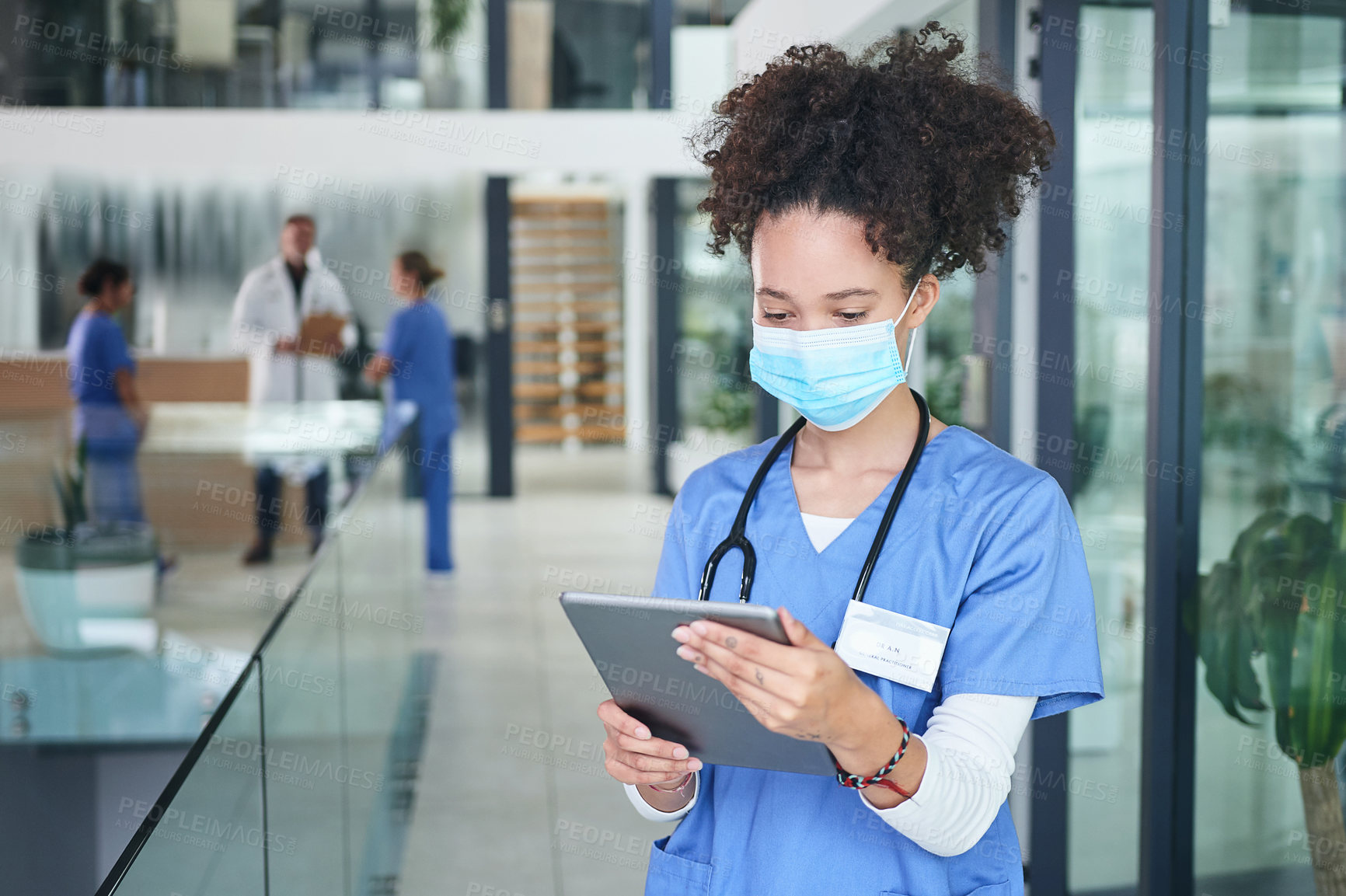 Buy stock photo Cropped shot of an attractive young nurse standing and wearing a face mask while using a digital tablet