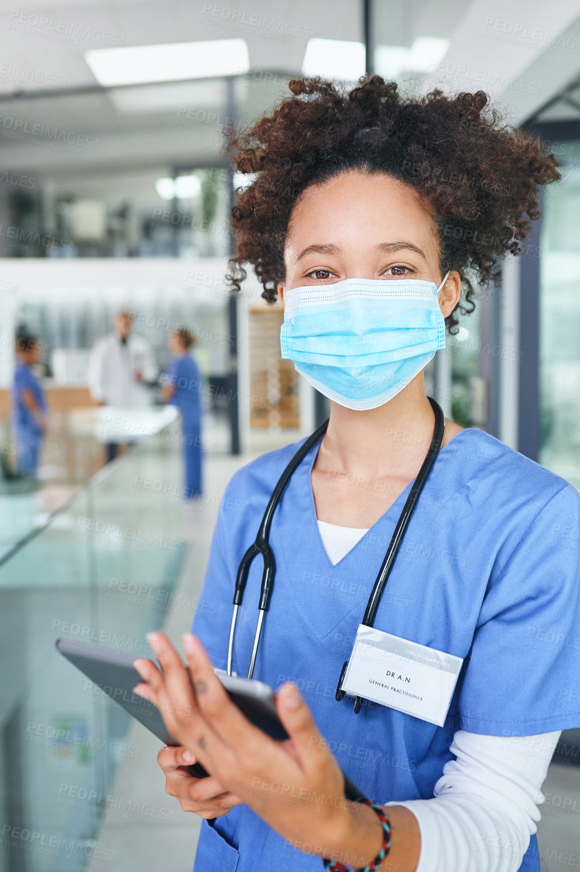 Buy stock photo Cropped portrait of an attractive young nurse standing and wearing a face mask while using a digital tablet