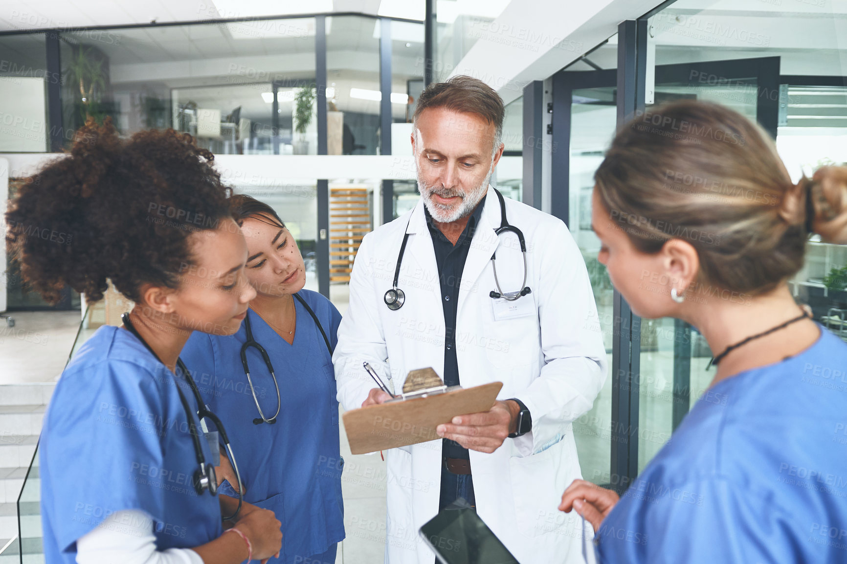 Buy stock photo Cropped shot of a handsome mature doctor standing with his nurses and using a clipboard during a discussion