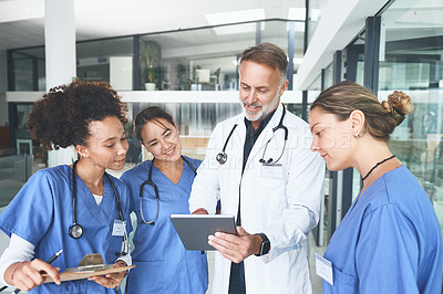 Buy stock photo Cropped shot of a handsome mature doctor standing with his nurses and using a digital tablet during a discussion