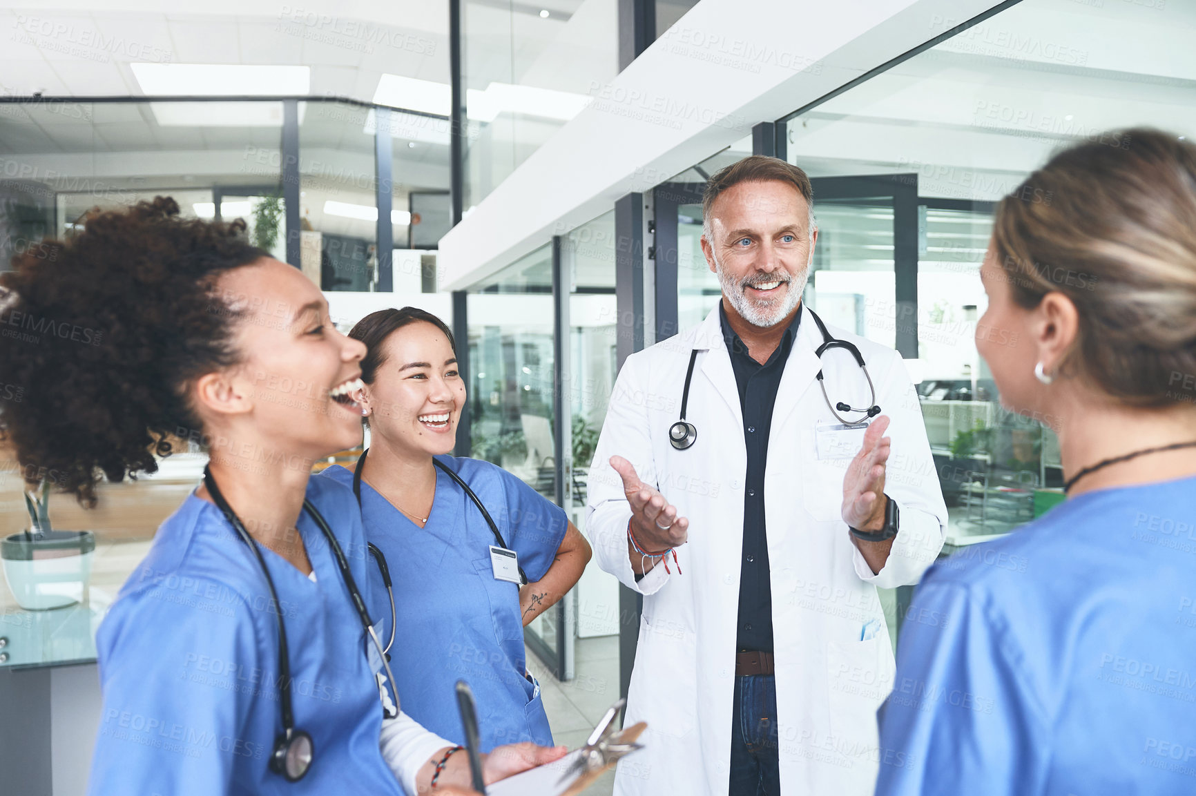 Buy stock photo Cropped shot of a handsome mature doctor standing with his nurses and having a discussion in the clinic