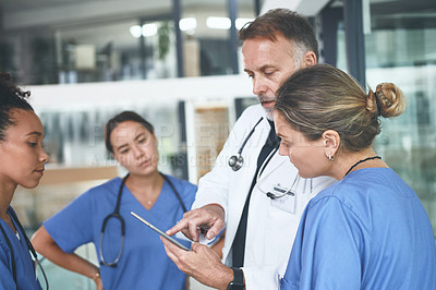 Buy stock photo Cropped shot of a handsome mature doctor standing with his nurses and using a digital tablet during a discussion