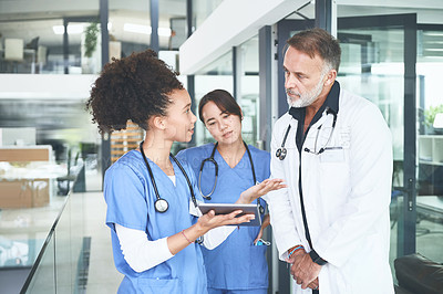 Buy stock photo Cropped shot of a handsome mature doctor standing with his nurses and using a digital tablet during a discussion