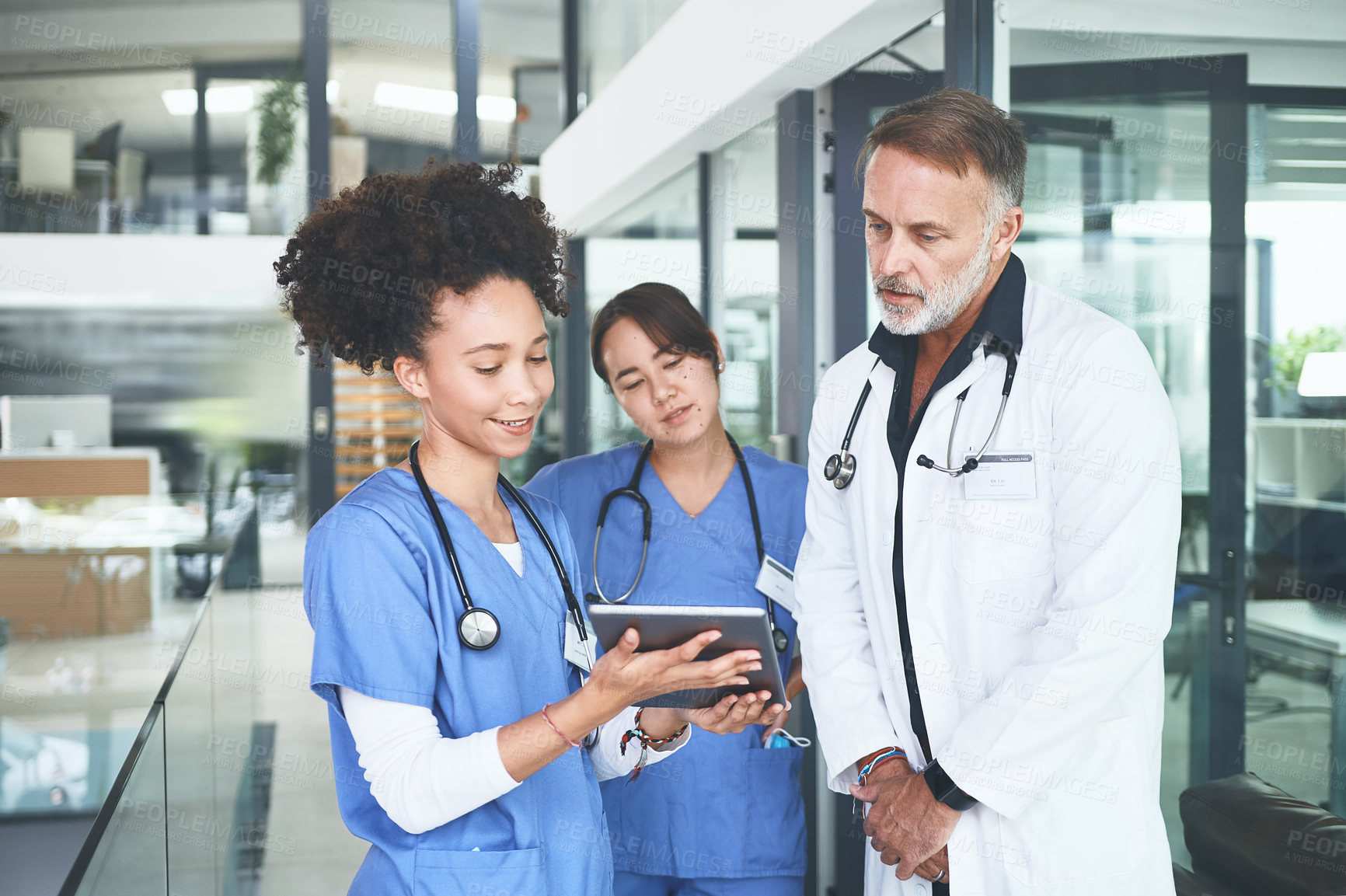 Buy stock photo Cropped shot of a handsome mature doctor standing with his nurses and using a digital tablet during a discussion