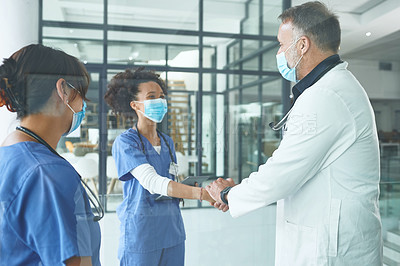 Buy stock photo Cropped shot of a handsome mature doctor standing and shaking a nurse's hand in the clinic
