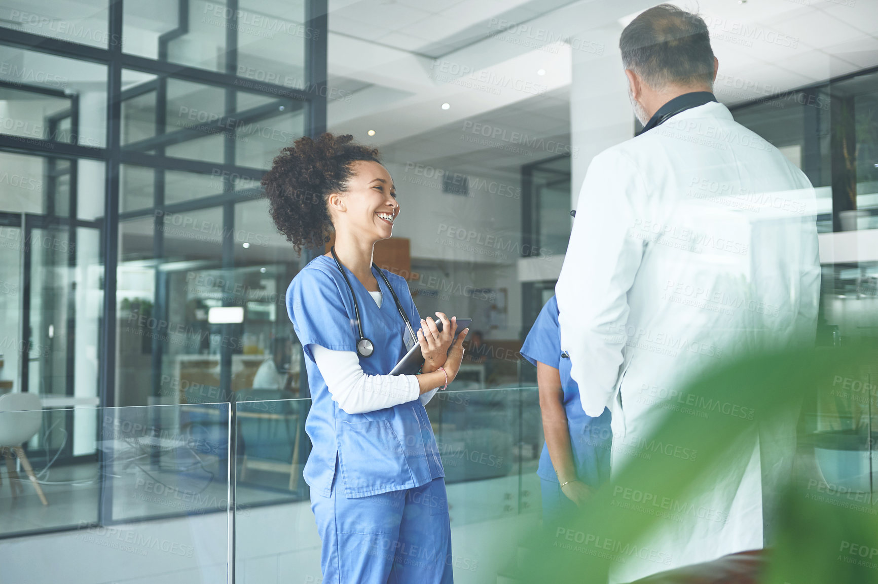 Buy stock photo Cropped shot of an attractive young nurse standing with coworkers and having a discussion in the clinic