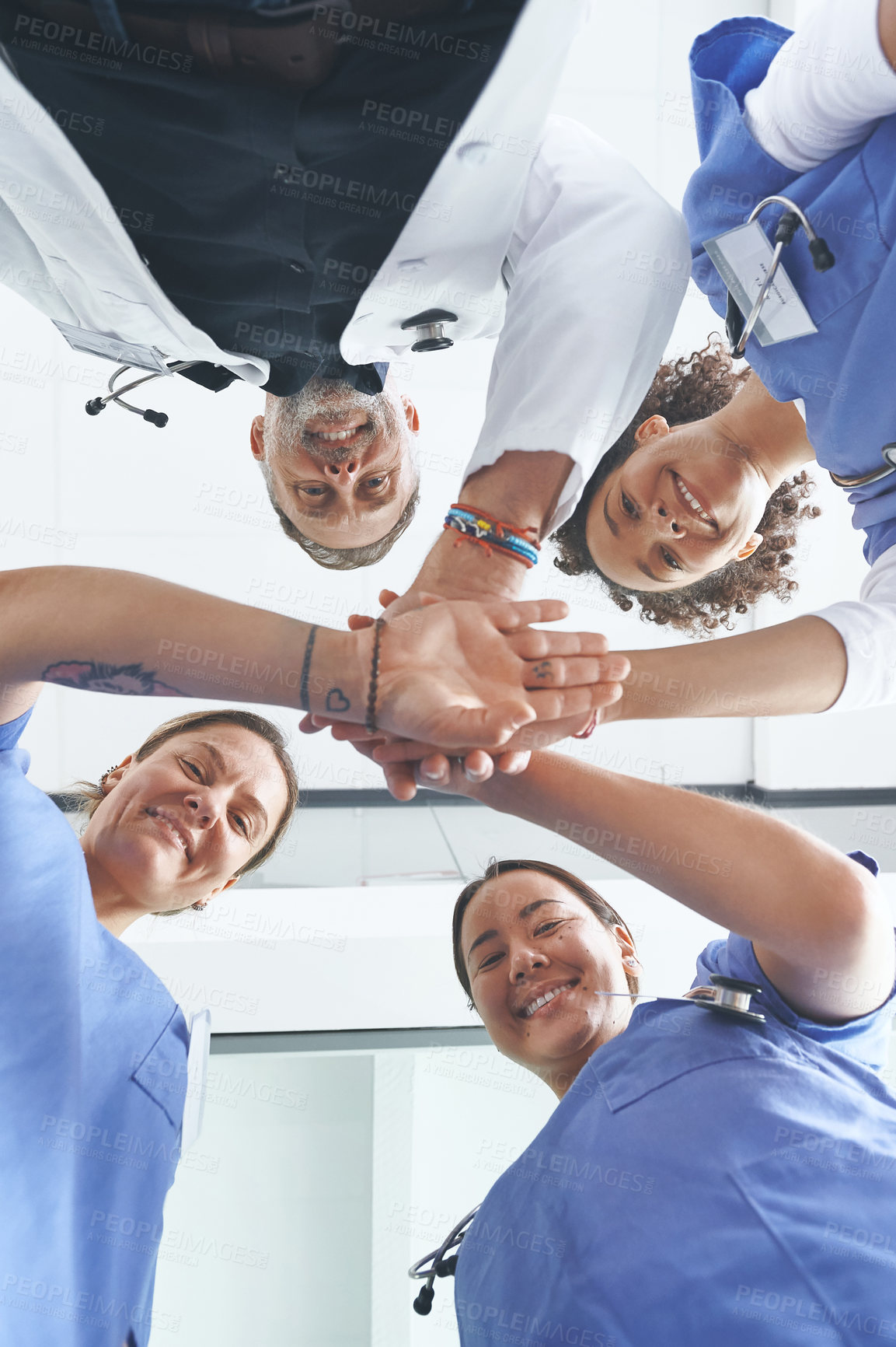 Buy stock photo Low angle portrait of a diverse group of healthcare professionals standing huddled together with their hands piled in the middle