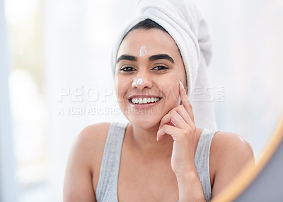 Buy stock photo Shot of happy young woman applying facial moisturiser in front of her mirror