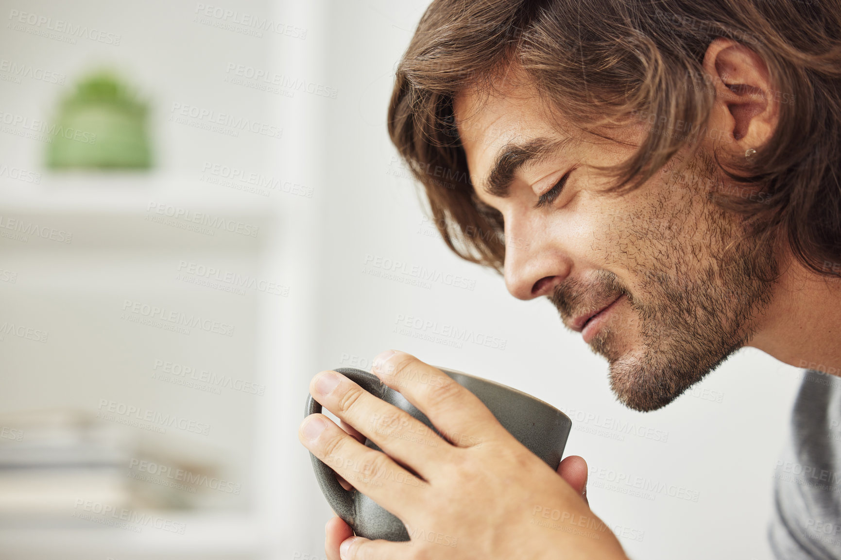 Buy stock photo Shot of young man drinking a cup of coffee happily.