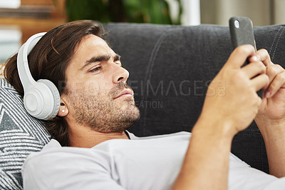 Buy stock photo Man, headphones and phone for music on couch, relax and listen to song and scroll on social media. Male person, home and rest app for playlist or conversation, text and podcast audio for streaming