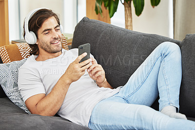 Buy stock photo Man, headphones and phone for audio on couch, relax and listen to song and scroll on social media. Male person, home and sound app for playlist or conversation, text and podcast for streaming online