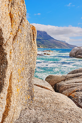 Buy stock photo Stunning seaside location for a summer holiday in Cape Town. Boulders at a beach with ocean waves and water washing over rocks at the coast with mountain and blue sky with clouds in the background