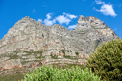 Buy stock photo Below view of majestic mountains with bushes growing below and cloudy blue sky copy space above. Nature landscape of mountain rock outcrops with wild green plants during a bright and beautiful day