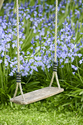 Buy stock photo Old wooden swing in a garden with blue flowers and grass in a lush backyard. Peaceful scene of a forgotten child playground with vibrant wild bluebells and overgrown lawn in spring with copy space