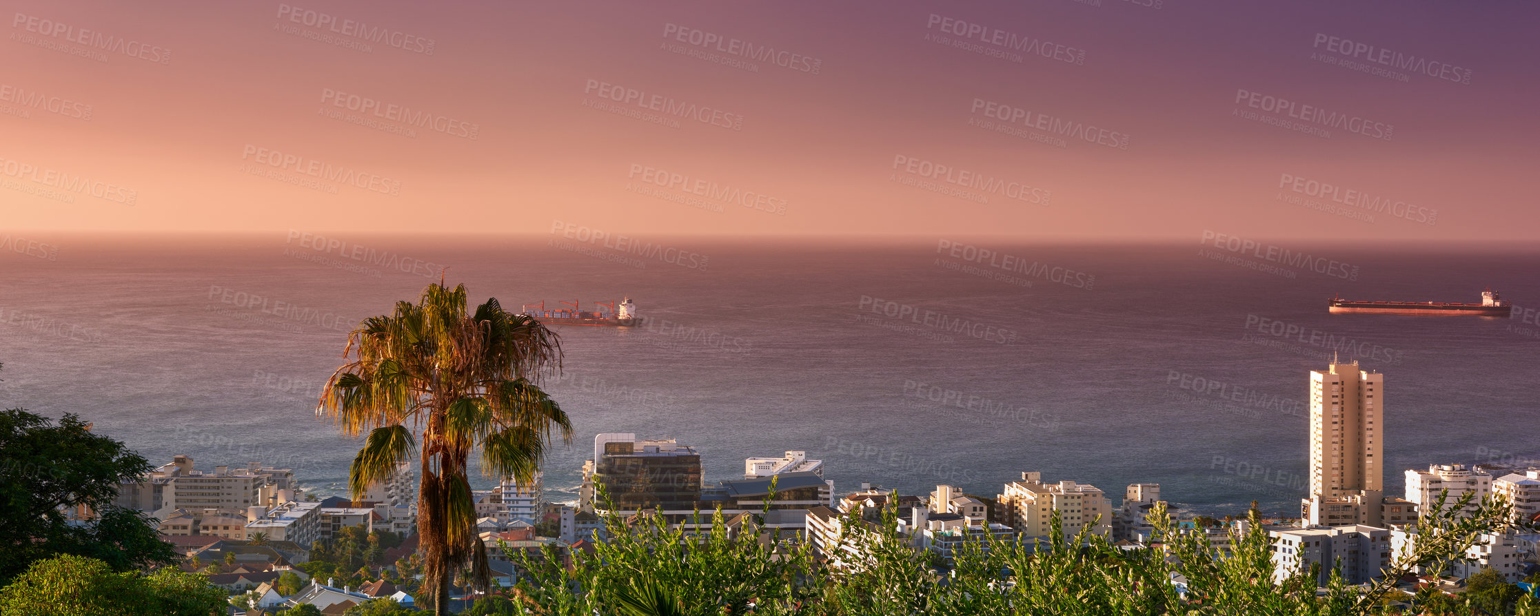 Buy stock photo High angle seascape of the ocean and urban buildings on the city beachfront in a tourist holiday location in summer. Aerial view of Cape Town, South Africa with lush trees and plants after sunset