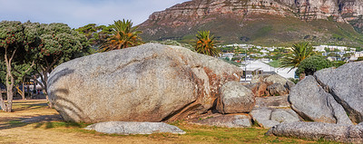 Buy stock photo Landscape view of beach rocks and boulders with lush trees and grass. Scenic mountain hills in the background with clear blue sky and during sunset on a beachfront in topical weather during summer