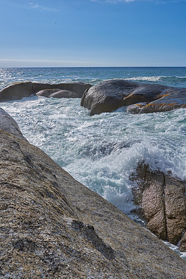 Buy stock photo Landscape view of boulders on the ocean and water during summer. Scenic view of waves crashing into the rocks in the sea against a clear blue sky. Beautiful nature views at the beach on the coast