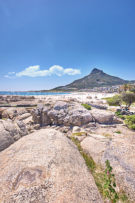 Buy stock photo Large rocks at a beach near a mountain with a blue sky background on a hot summer day. The landscape of a rocky sea or ocean shore during spring break. Sunny coastal land with large stones