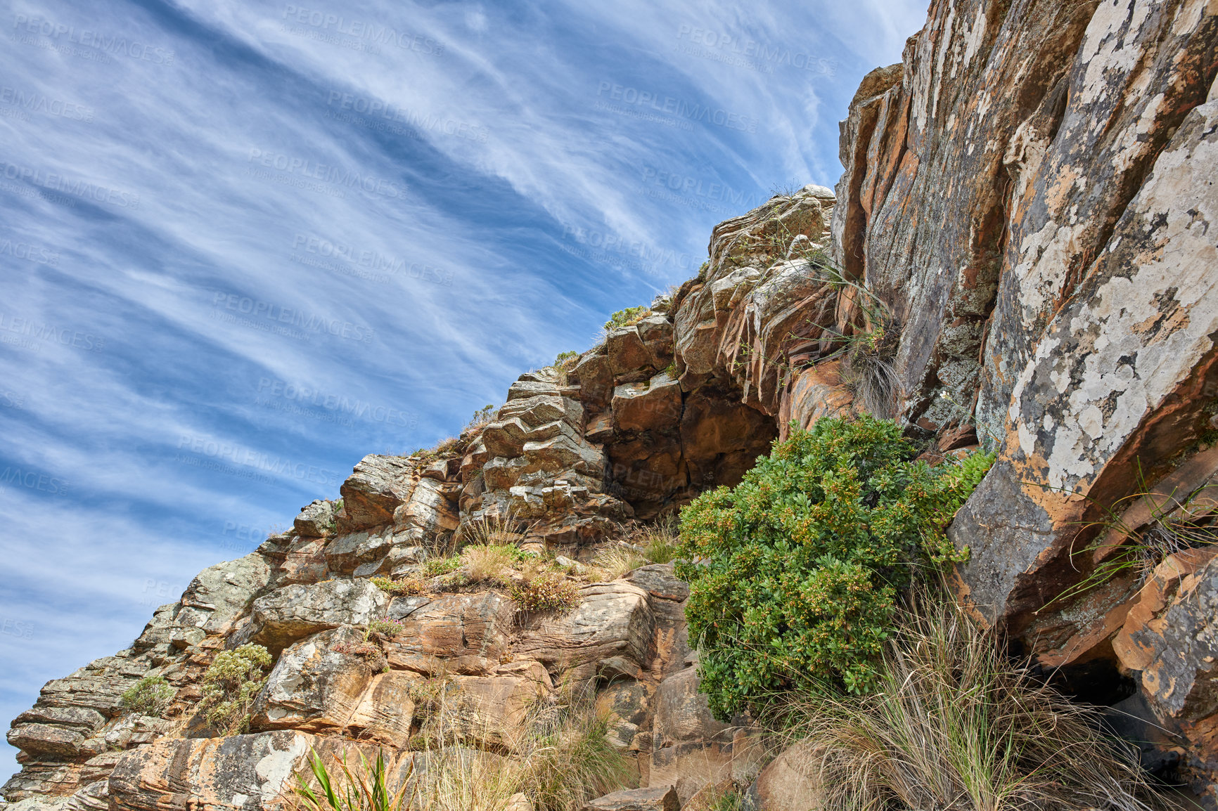 Buy stock photo Copy space on a rocky mountain with plants and shrubs growing against a cloudy sky background. Rugged, remote and quiet landscape with boulders and stones on a cliff to explore during a scenic hike